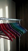 Colorful clothes hangers arranged on metal rod in modern closet with natural sunlight creating shadows on wall for wardrobe organization and storage.