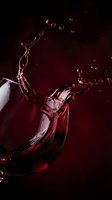 Red wine splashing from glass with dynamic droplets against dark burgundy background creating elegant motion for luxury beverage advertising.