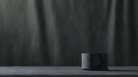 Minimalist dark composition featuring cylindrical object on reflective surface against black background. Dramatic lighting creates moody atmosphere.