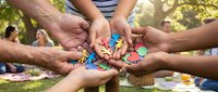 Diverse group of people joining hands together outdoors in park, showing unity, teamwork and community support during outdoor gathering or team building event.