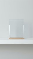 Minimalist clear acrylic display stand with wooden base on white surface against neutral gray wall for product presentation and retail showcase.