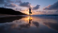 Woman practicing yoga tree pose on beach at sunset with reflection in wet sand, dramatic clouds and mountain silhouette create serene coastal atmosphere.
