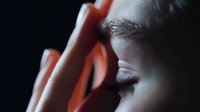 Close up portrait showing woman's eye and hand in dramatic lighting with deep shadows, creating mysterious and emotional atmosphere for beauty and fashion concepts.