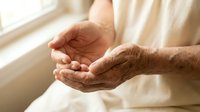 Elderly hands cupped together in gentle prayer or meditation pose, showcasing wrinkled skin and peaceful gesture in soft natural window light.