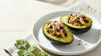 Halved avocado filled with seasoned ground meat, topped with diced red onion and fresh cilantro, served on white plate for healthy meal preparation.