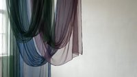 Sheer fabric drapes in layered teal, purple, and gray tones hanging against white wall, suitable for interior design and home decor projects.