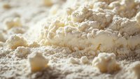 Fresh white wheat flour scattered and piled with soft focus macro photography showing fine powder texture in warm natural lighting for baking and cooking concepts.