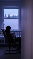 Mother silhouette holding baby in rocking chair by window during twilight hour creating peaceful nursery scene for parenting and childcare concepts.