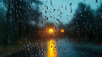Raindrops on window glass with blurred city lights creating bokeh effect in evening. Moody atmospheric scene with water droplets reflecting golden glow.