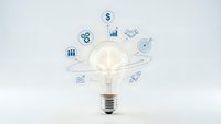 Glowing light bulb with business icons floating around representing innovation, creativity, and entrepreneurial ideas on white background.