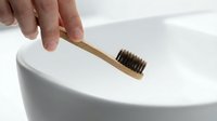 Hand holding eco-friendly bamboo toothbrush with natural bristles over white ceramic sink in modern bathroom for sustainable oral hygiene routine.