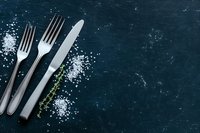 Silver forks and knife with sea salt crystals and thyme on dark slate surface, top view with copy space for restaurant menu design.