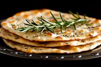 Stack of crispy flatbread garnished with fresh rosemary sprigs and herbs on dark plate against black background, macro food photography for restaurant menu.