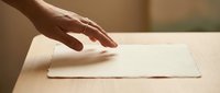Woman's hand reaching toward blank white envelope on wooden table, suitable for business correspondence and mail concepts.