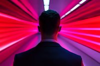 Back view of businessman in dark suit standing in futuristic corridor with dramatic red neon lighting and perspective lines creating dynamic atmosphere.