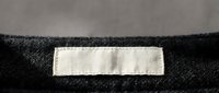 Blank white clothing label sewn on dark fabric seam, ready for custom branding and garment identification in fashion manufacturing and textile industry.