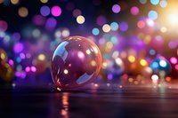 Clear glass bubble on dark surface with colorful defocused bokeh lights creating magical atmosphere. Festive background with dreamy blurred circles.