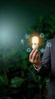 Businessman holding glowing energy efficient lightbulb with green eco icons and plant background representing sustainable business solutions and environmental innovation.