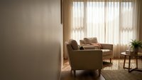 Modern living room interior with comfortable armchairs and natural sunlight streaming through sheer curtains creating warm atmosphere for home decor.