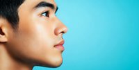 Profile view of young Asian male model with clear skin against vibrant turquoise background, showing facial features in sharp detail for beauty and skincare marketing.