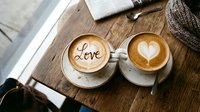Two cappuccinos with latte art on a rustic wooden table, one with a heart and one with the word Love, romantic cafe atmosphere.