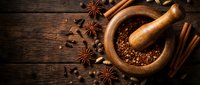 Wooden mortar and pestle with crushed spices on rustic dark wood background. Aromatic star anise, cinnamon sticks and peppercorns for cooking and seasoning.
