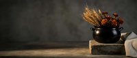 Autumn harvest arrangement with wheat stalks and dried flowers in black ceramic pot on rustic wooden surface against dark textured background.