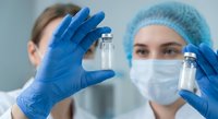 Female scientist in protective mask and gloves examining medical vials in laboratory for pharmaceutical research and drug development testing.