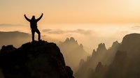 Silhouette of triumphant hiker with raised arms standing on mountain peak at sunrise, celebrating success and achievement with dramatic landscape view.