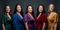 Five diverse women in colorful wrap dresses standing together smiling, representing friendship, teamwork and female empowerment in professional setting.