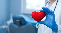 Healthcare professional in blue gloves holding red heart symbol in modern medical facility representing cardiology care and heart health services.