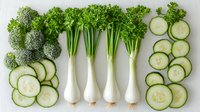 Fresh green vegetables arranged in neat rows on white background - broccoli florets, sliced cucumbers, and celery stalks with roots. Clean eating and healthy food concept.