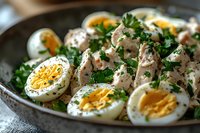 Fresh tuna salad with halved boiled eggs and chopped parsley garnish on rustic plate, creamy mayonnaise dressing and cracked black pepper seasoning.