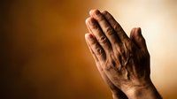 Elderly hands pressed together in prayer against warm golden background, expressing faith, hope, and spiritual devotion.