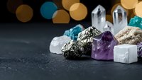 Collection of healing crystals and gemstones including amethyst, quartz, and pyrite arranged on dark surface with warm bokeh lights for meditation and wellness.