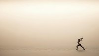 Athletic woman running across vast desert sand dunes during golden hour creating minimalist composition with copy space for motivational content.