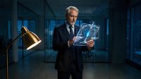 Senior businessman in suit holding futuristic holographic tablet with glowing interface in modern office environment at night.
