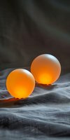Two translucent amber spheres with glowing interiors rest on gray fabric against a dark textured backdrop, suitable for wellness, spa, and alternative therapy design projects.