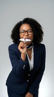 Professional African American businesswoman in navy suit holding paper airplane with joyful expression against gray studio background.
