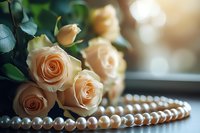 Delicate peach roses with pearl necklace on wooden surface in soft natural light. Romantic floral composition with bokeh effect creates elegant mood for wedding design.