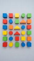 Colorful wooden geometric shapes including cubes, cylinders, spheres and triangles arranged in organized rows on neutral background for educational and design projects.