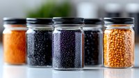 Assorted legumes and seeds in glass jars with metal lids, including lentils, beans, and peas for cooking, storage, and pantry organization.