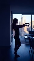 Young woman in black dress dancing gracefully in a dimly lit modern apartment with city skyline glowing through large windows at dusk.