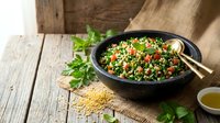 Fresh tabbouleh salad with parsley, tomatoes and quinoa served in black bowl on rustic wooden table with golden chopsticks for healthy Mediterranean cuisine.