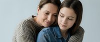 Caucasian mother and teenage daughter sharing a tender embrace, eyes closed, expressing love, trust, and emotional bond on light background.