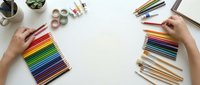 Hands arranging colorful pencils and art supplies on white desk for creative drawing and design projects. Flat lay workspace with organized materials.