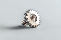 Metal gear wheel with bolt on light gray background, industrial machinery part showing mechanical engineering detail and precision manufacturing.