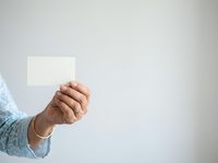 Male hand holding blank white card against neutral background for mockup and branding purposes.