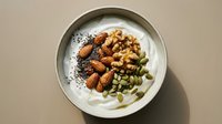 Creamy yogurt bowl topped with roasted almonds, walnuts, pumpkin seeds and poppy seeds for healthy breakfast or snack preparation.