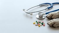 Medical stethoscope with colorful pills and latex gloves on white background for healthcare and pharmaceutical concepts.